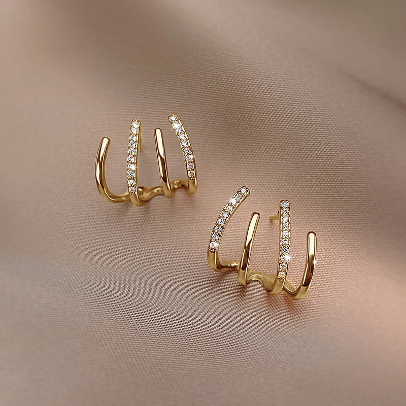 Pair of gold four-claw earrings on beige fabric, one showing its front, the other angled to the side 9
