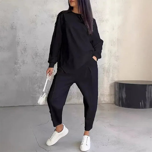 Model wearing the black set with a hand in her pocket, carrying a small white bag and white trainers. 2
