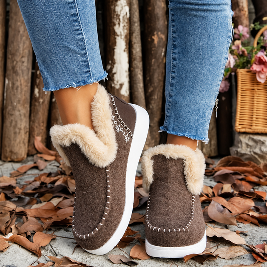 Rear three-quarter view of brown textured slip-ons with plush trim and snowflake embroidery, worn outdoors 2