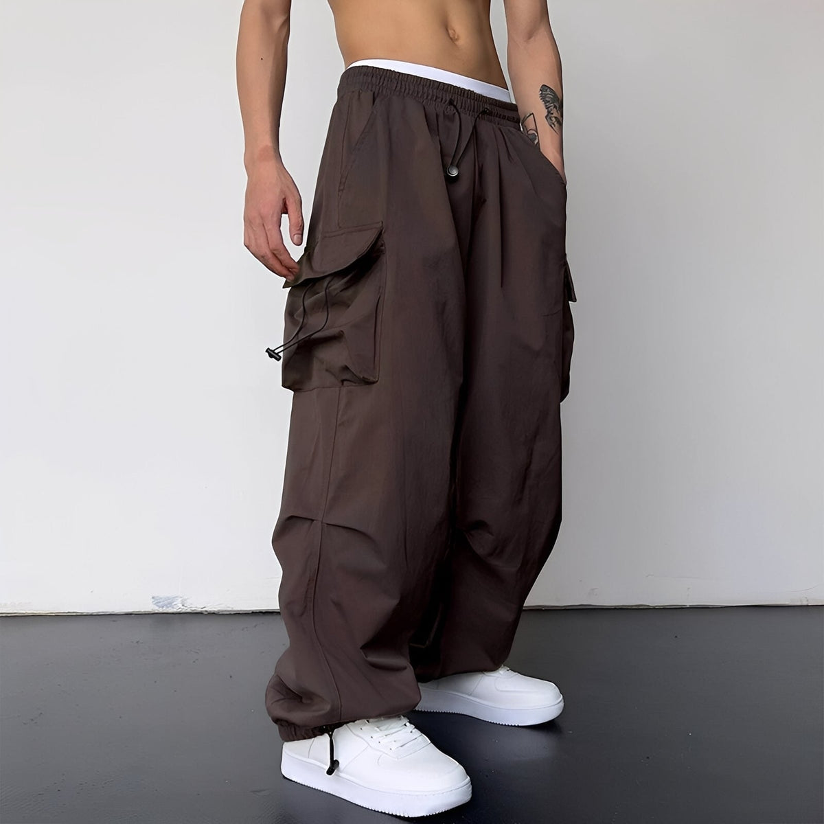 Model wears the baggy cargo trousers in dark brown with white trainers, side view 6