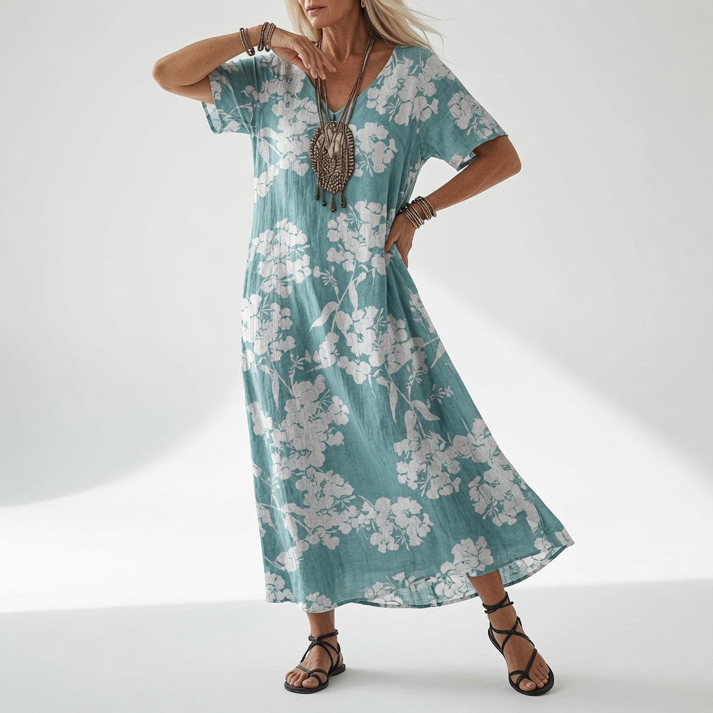 Model in a loose teal dress with a white hydrangea-style floral print, styled with a beaded pendant necklace and black strappy sandals. 4