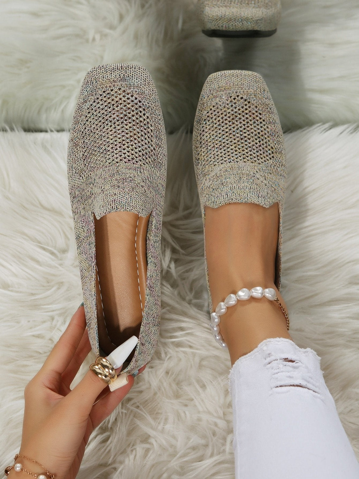 Top-down view of speckled beige knit slip-on shoes with perforated mesh toes, one worn with a pearl anklet, one held to show the cushioned footbed. 21