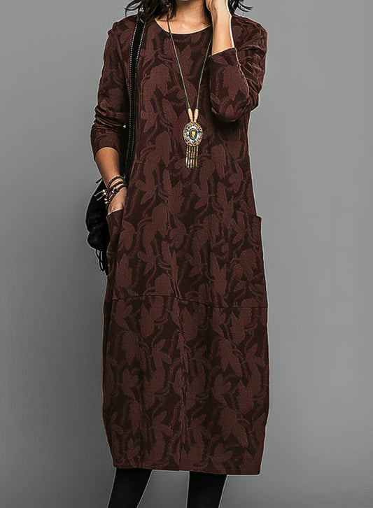 Model wearing the dress in deep burgundy with a tonal leaf pattern, pendant necklace and black bag 2
