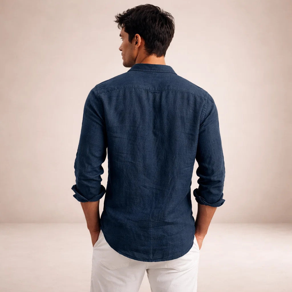 Back view of a navy linen shirt on a model with hands in white trouser pockets, showing the yoke and rolled sleeves. 13