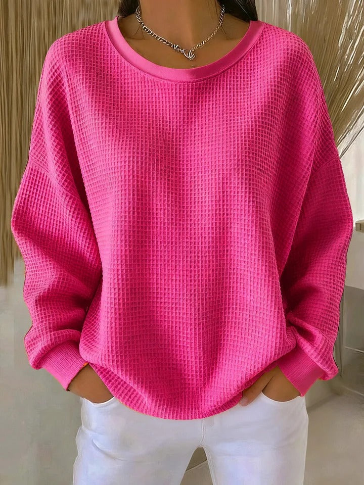 Model wearing the waffle-knit jumper in hot pink, with a round neckline and relaxed sleeves, over white trousers. 9
