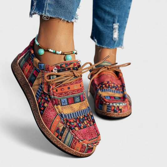 Front three-quarter view of red and orange patterned lace-up shoes with a cork-style sole, worn with frayed jeans and a turquoise beaded anklet. 1