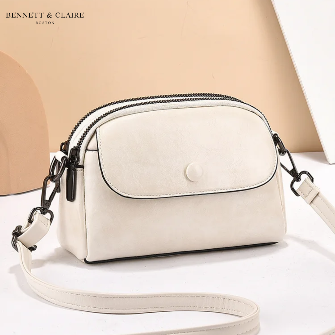 Cream-white version of the crossbody bag, with a smooth front flap, black edging and black metal clips on the strap. 4