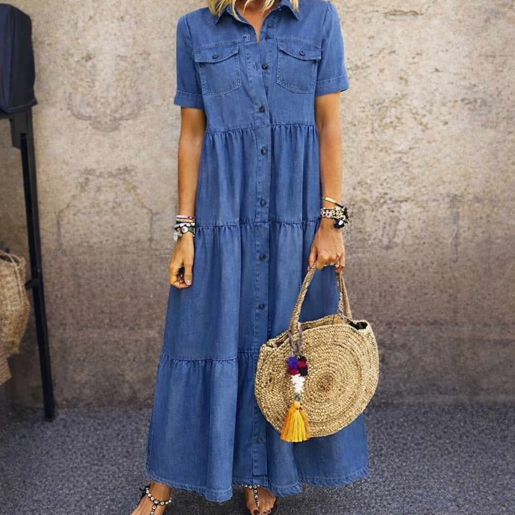 Model wears the same tiered, button-front dress in a darker mid-blue denim with chest pockets, carrying a round woven straw bag. 2