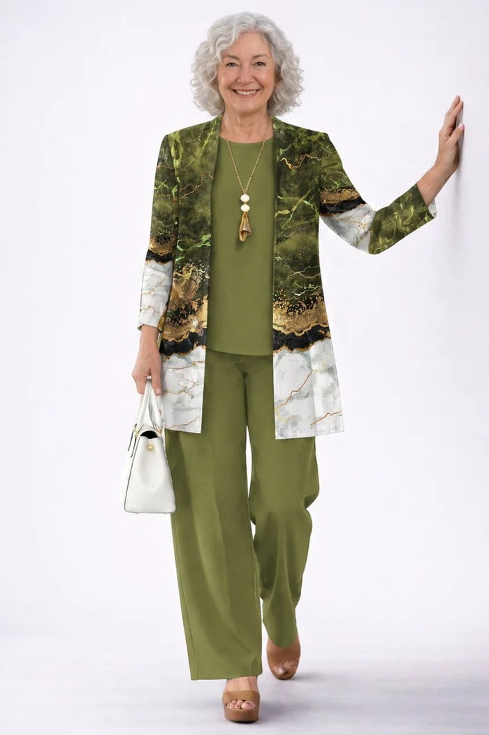 Smiling model with grey curly hair in a green set with a marble-print cardigan, leaning on a wall 12
