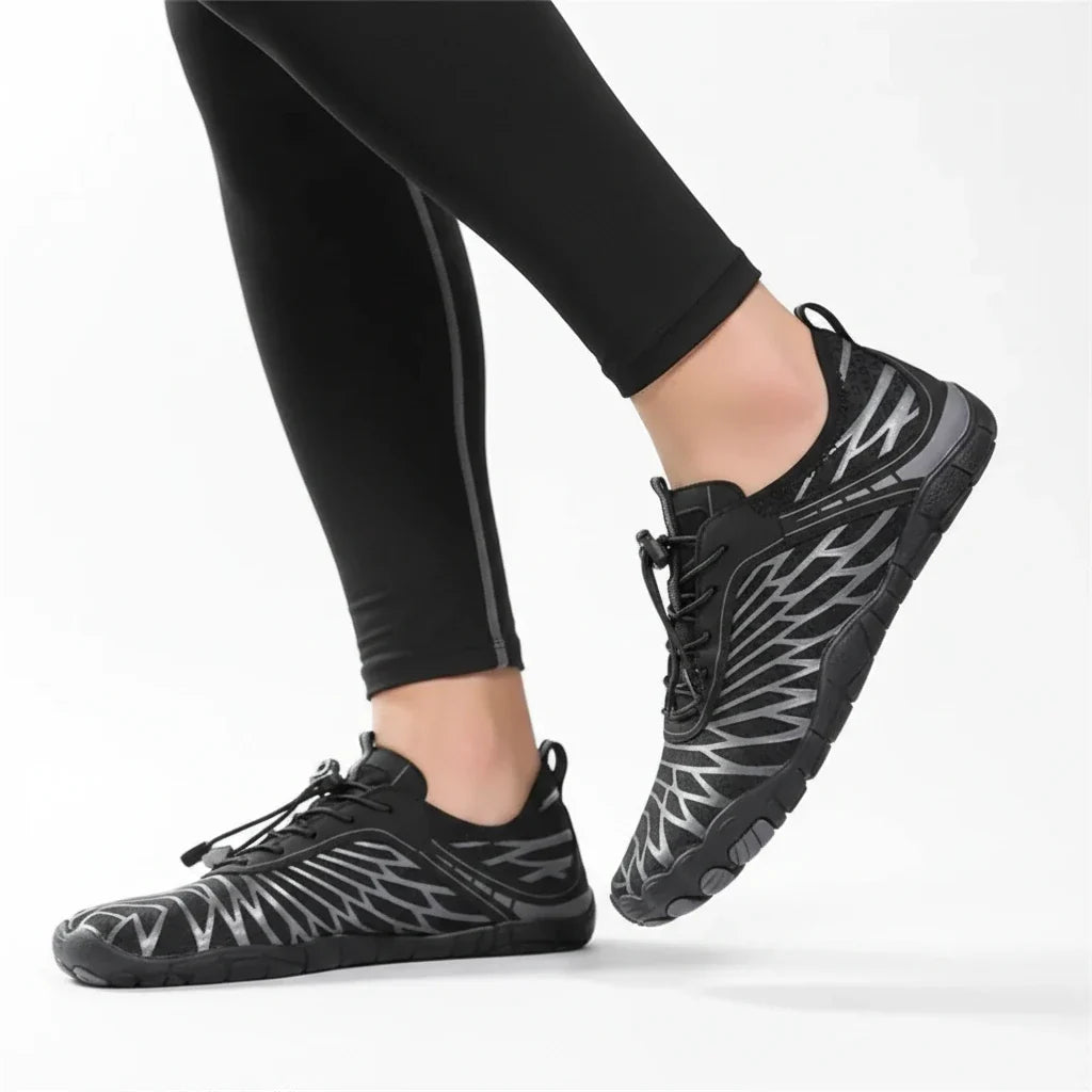 Model in black leggings wearing black barefoot shoes with grey line pattern, toggle laces and flat sole, mid-stride on white background. 21