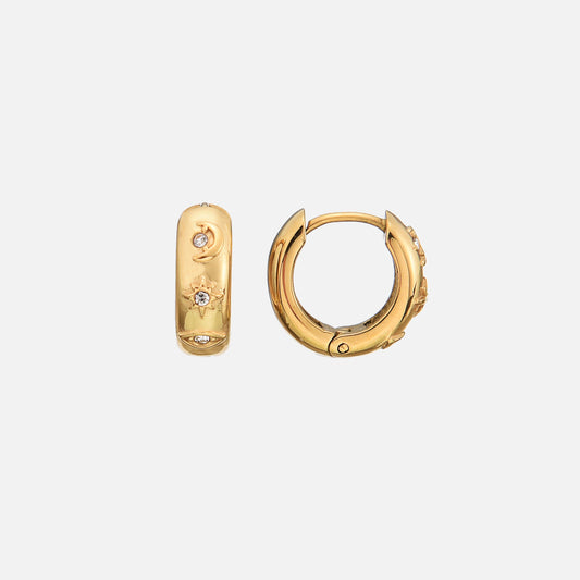 Pair of gold-tone huggie hoops on a plain pale background, one seen from the side and one from the front, with moon, star and eye motifs set with small clear st 1