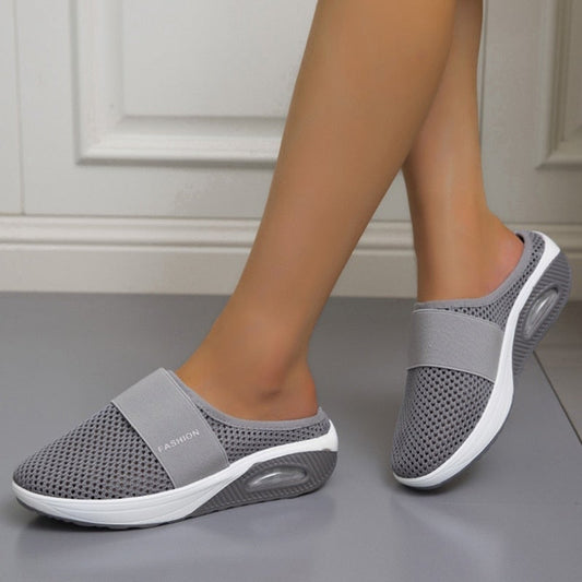 Pair of grey mesh slip-on mules worn by a model walking on a grey floor 2