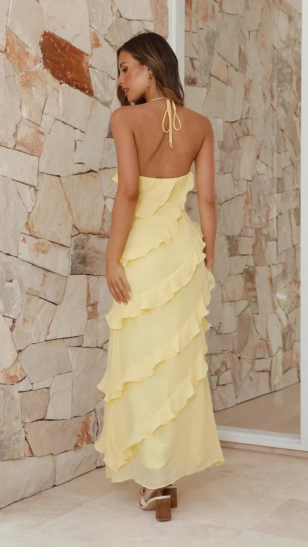 Back view of the dress on a model, showing the open back, halter tie and tiered ruffles 2