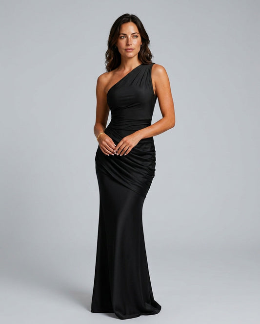 Model in the black satin maxi dress, front view, one shoulder with ruched draping across the hip, hands clasped. 1