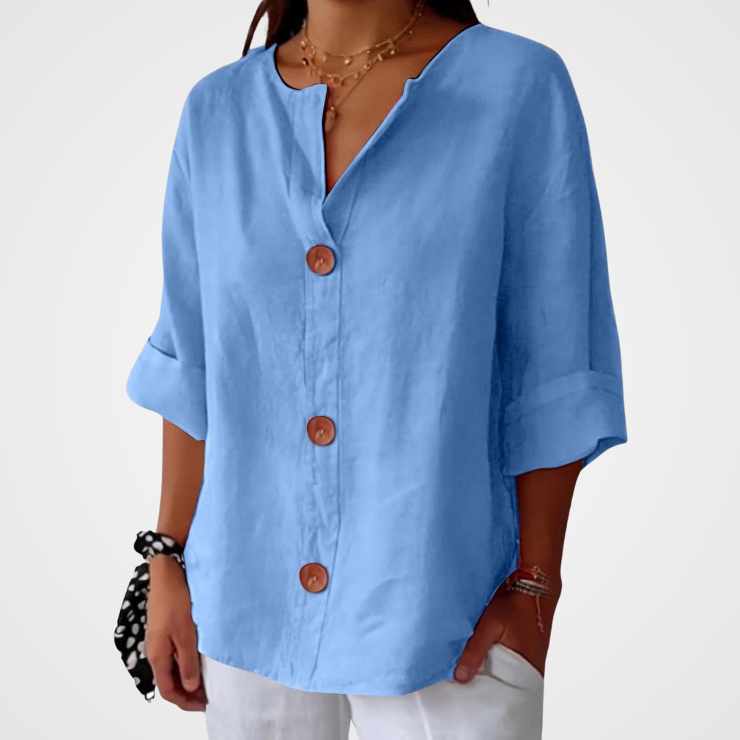 Light blue loose blouse worn by a model against a plain pale background, showing the V-neckline, three buttons and relaxed sleeves. 14