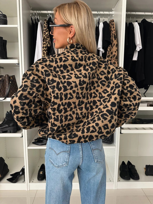 Back view of the leopard print bomber jacket on a model, showing the stand collar and full sleeves over blue jeans. 2