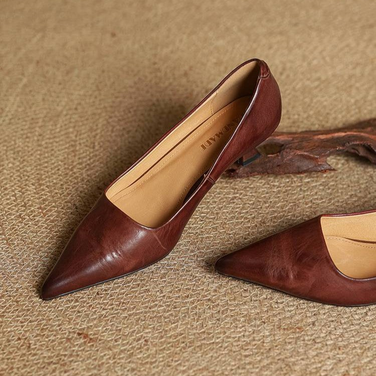 Brown leather pointed-toe pumps resting on a woven mat, showing the tan interior and low heel 22