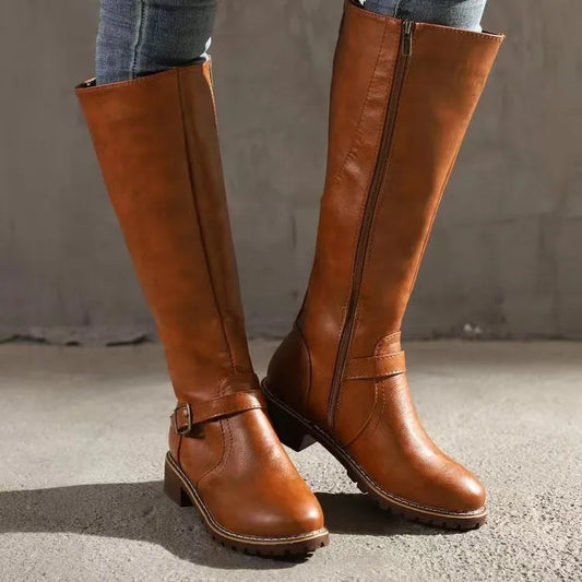 Tan knee-high boots worn with jeans, shown from the front with an inner-side zip and a buckled ankle strap. 1