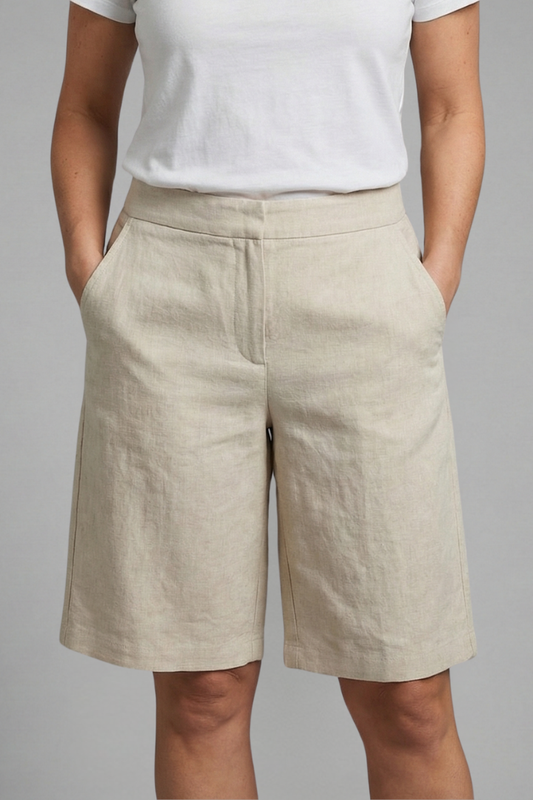 Close front view of knee-length shorts in a creased natural beige linen-look fabric, worn with a white tee, hands in pockets. 1