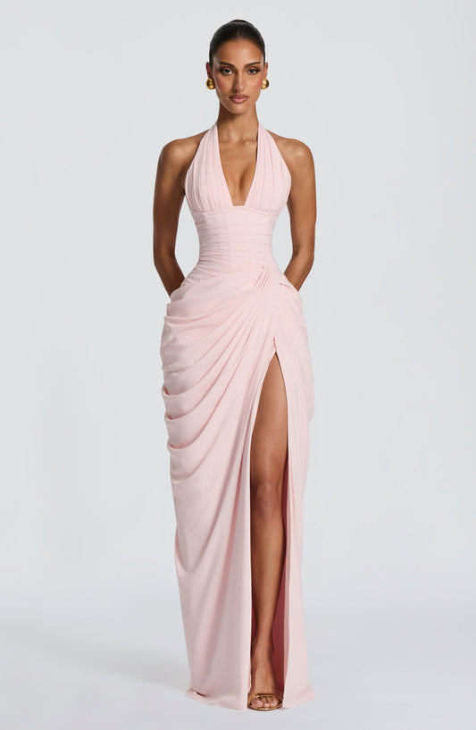 Model facing forward in the pale pink halterneck maxi dress, showing the pleated plunge neckline, corset waist and draped skirt with high slit. 1
