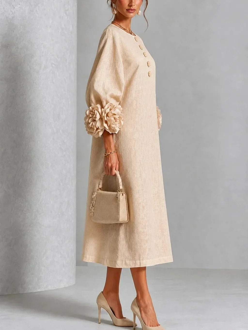 Side view of the beige dress on a model, showing the sleeve volume, flower cuff, flower buttons at the neckline and midi length. 8