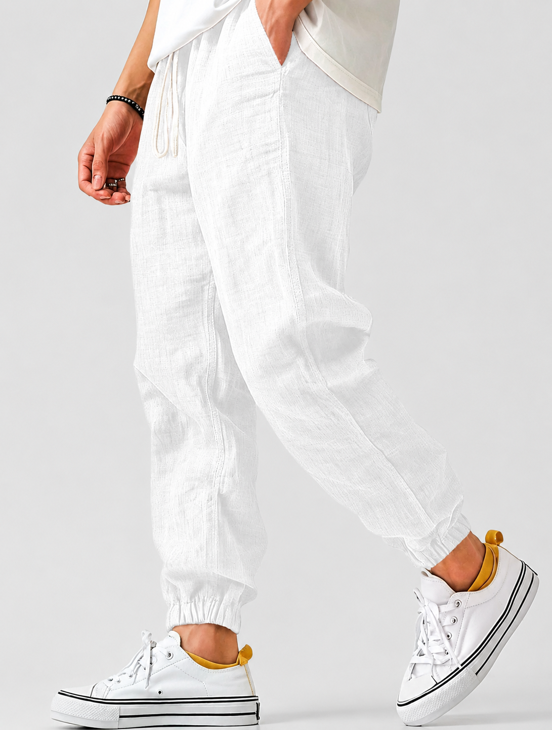 White jogger trousers worn by a model in a side view, with drawstring waist, textured fabric and elasticated ankles. 7