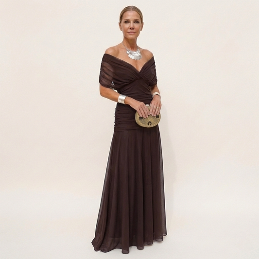 Full-length view of a dark brown chiffon version worn off the shoulder, with a ruched bodice and flowing skirt. 2