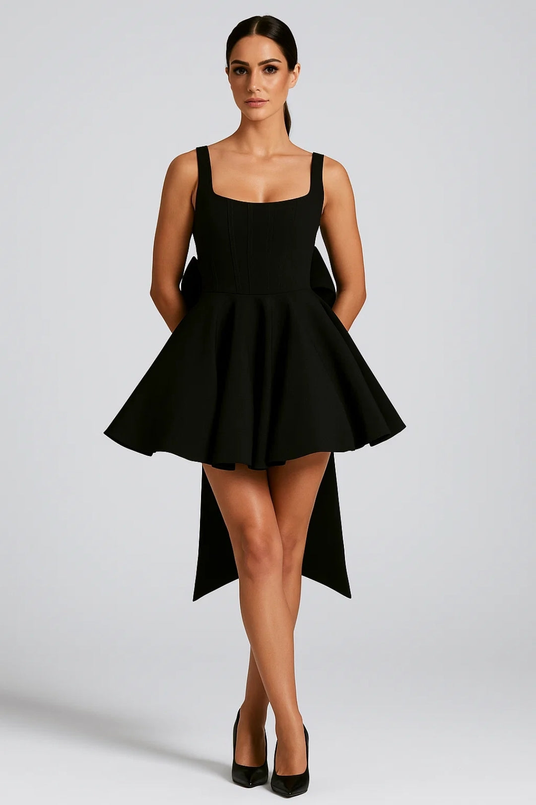 Model standing in the black version of the dress with black heels, bow tails behind 8
