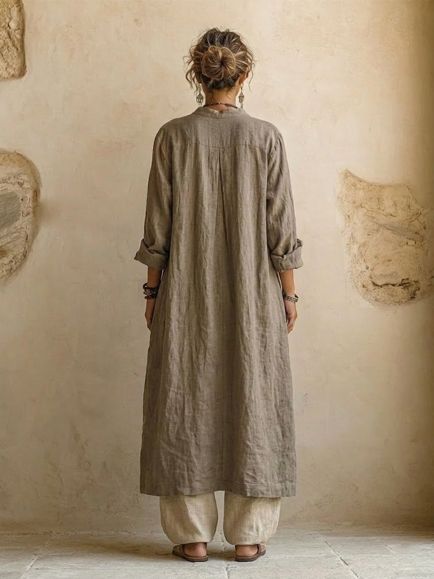 Back view of the long taupe linen coat with centre pleat and rolled sleeves, over beige trousers 5