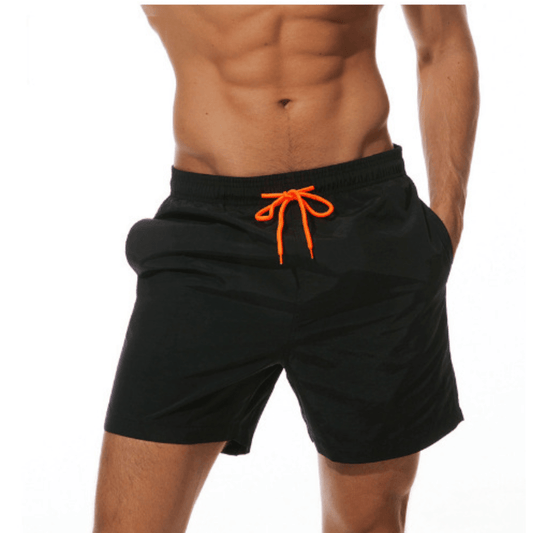 Model wearing black swim trunks with a bright orange drawstring, one hand in a side pocket, shown from the front. 1
