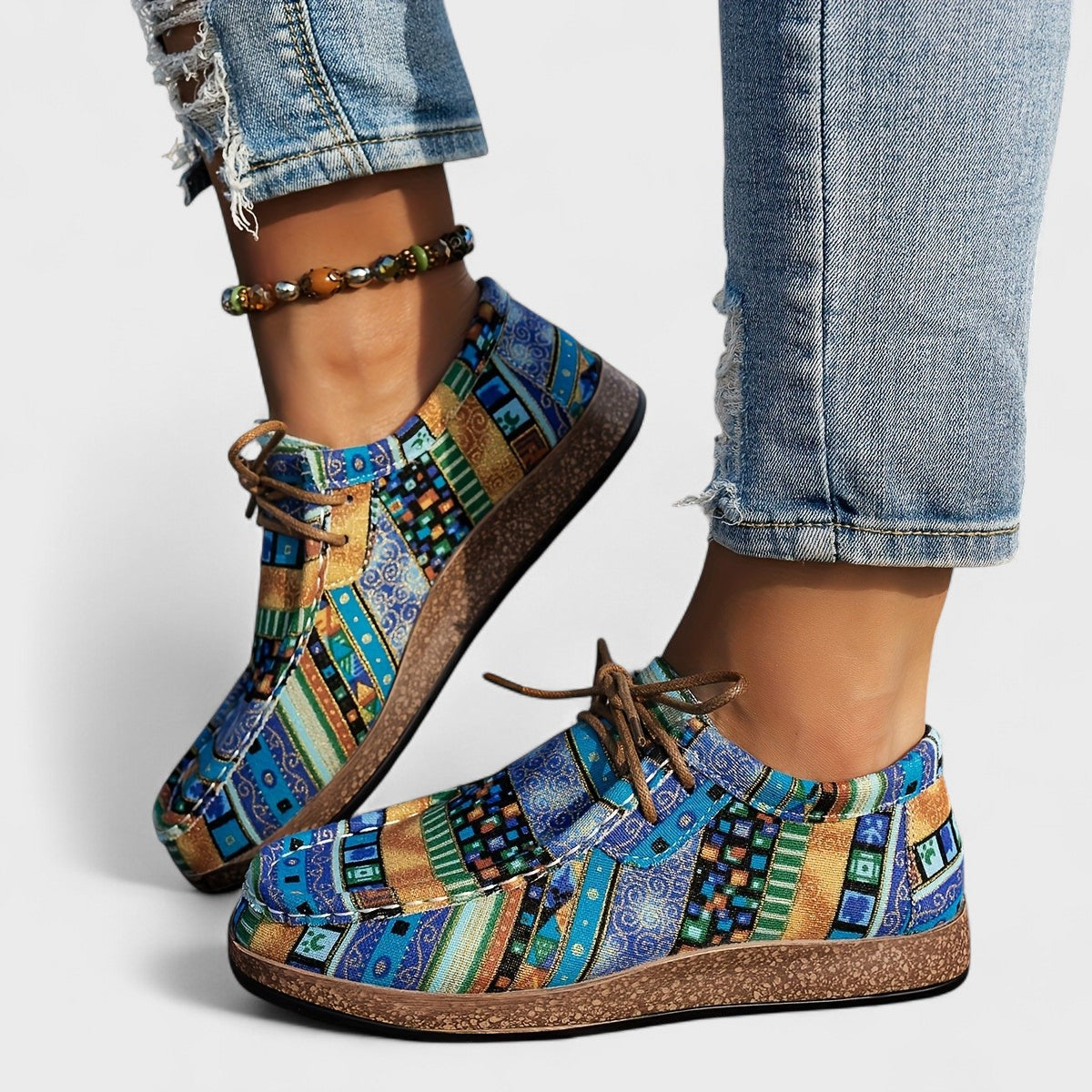 Model wearing blue, teal and mustard geometric-print lace-up shoes with a cork-effect sole, paired with ripped jeans and a beaded anklet. 6