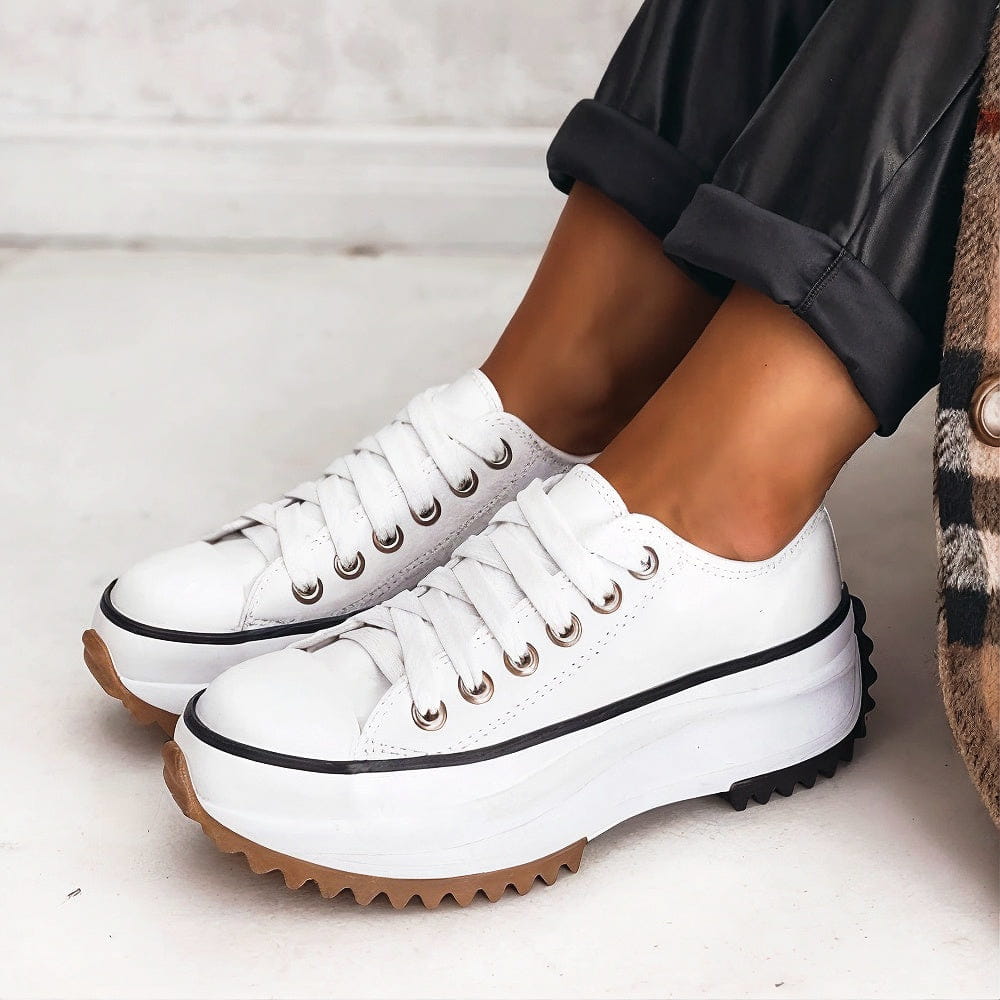 White lace-up platform trainers with a thin black stripe along the sole, worn with rolled black trousers. 4