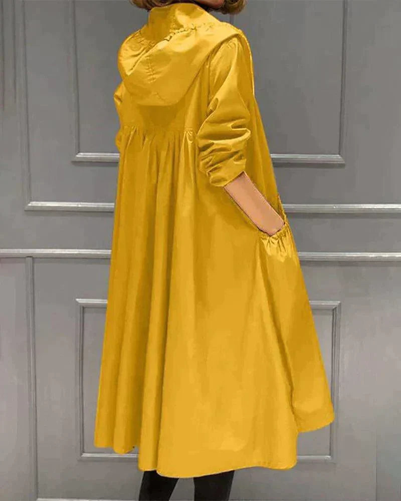 Back view of the mustard yellow hooded raincoat with a flared, pleated shape and hand in pocket 7