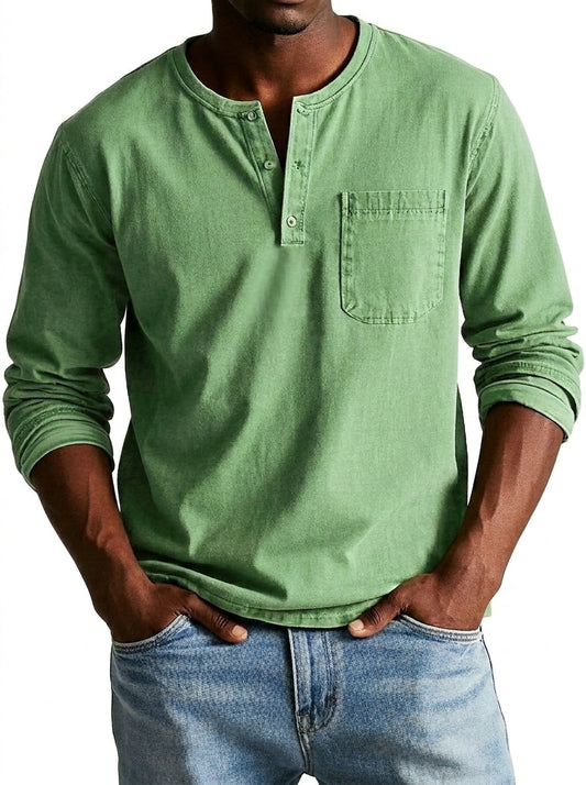 Model in light sage green henley with rolled sleeves and chest pocket, hands in the pockets of light blue jeans. 1