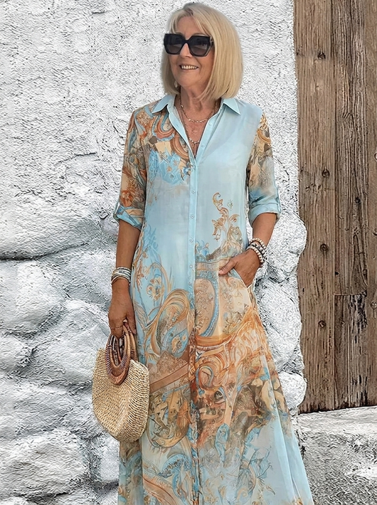 Model in a light blue button-through maxi dress with orange scrollwork print, rolled sleeves and a woven round handbag. 1