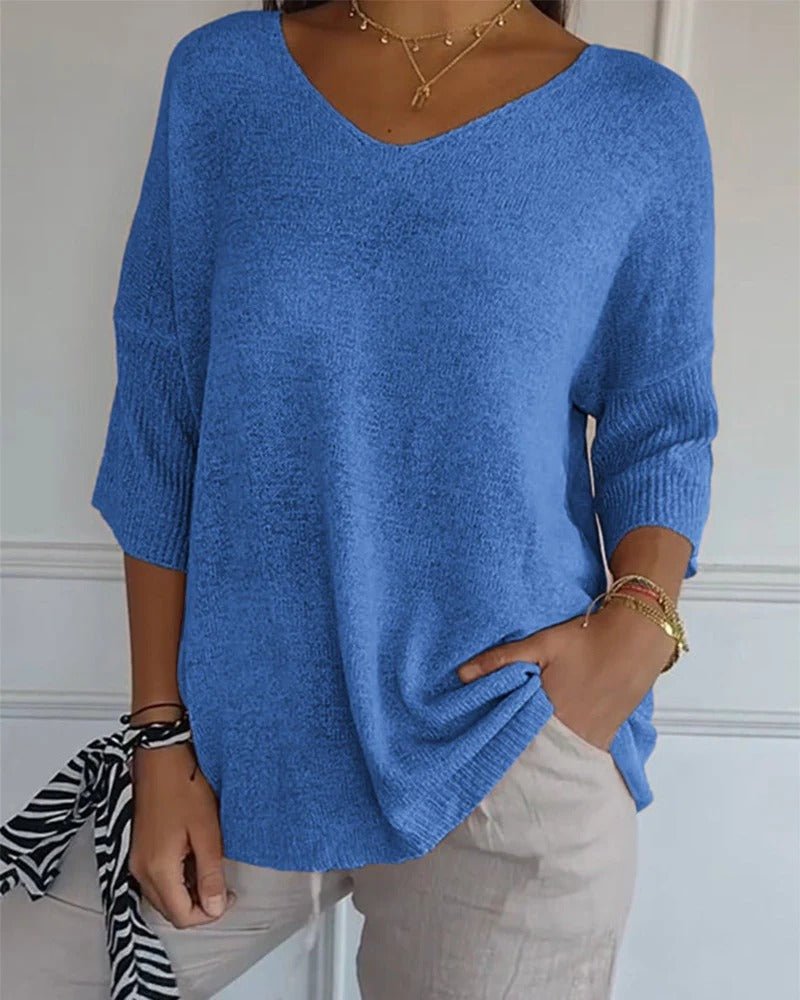 Model wearing a blue V-neck knit jumper with ribbed cuffs, paired with light trousers and gold jewellery 1