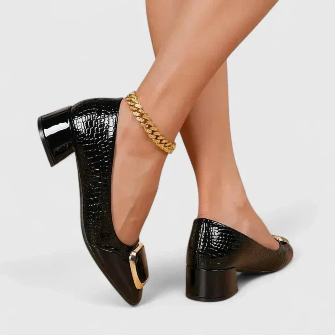 Black croc-effect block-heel loafers worn by a model with a gold ankle chain, showing the patent heel and gold trim. 7