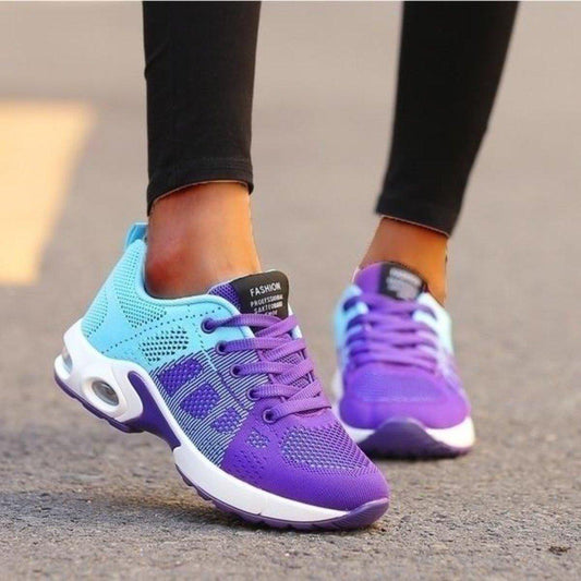 Worn on a tarmac road, a mesh trainer fades from turquoise to purple, with purple laces and a white air-cushion sole. 1