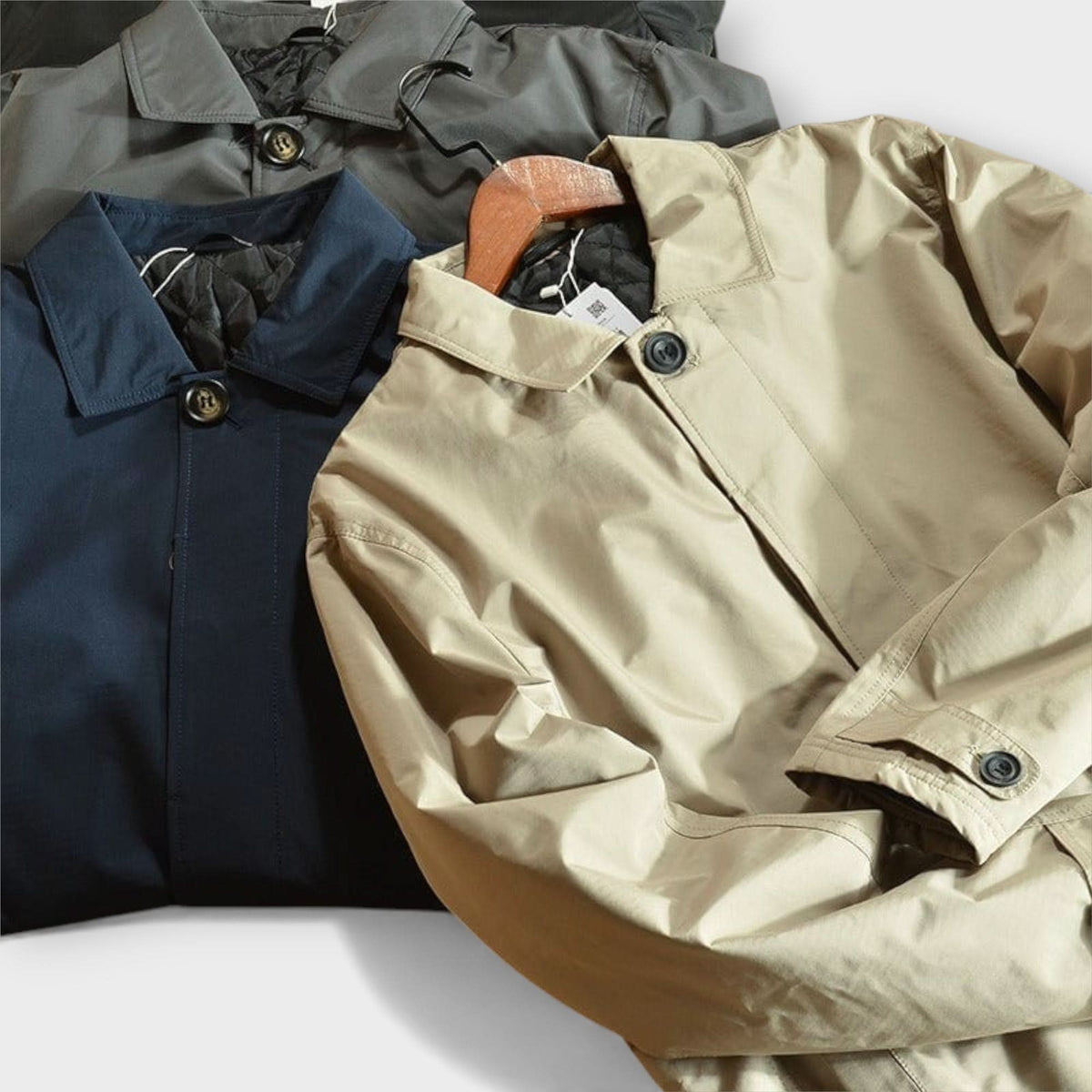 Flat lay of beige, navy and grey coats side by side showing collars, buttons and cuff tabs 9