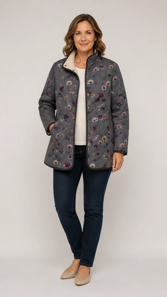 Woman wearing the grey floral quilted jacket open over a cream top, dark jeans and beige flats, full-length front view. 1