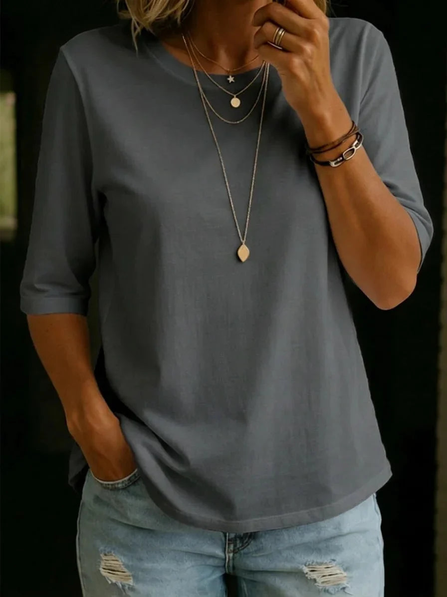 Woman wearing the slate grey half-sleeve crew-neck tee with layered gold necklaces, bracelets and ripped light-wash jeans. 7