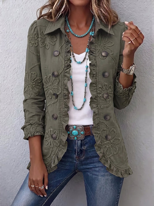 Woman wearing the olive green jacket open over a white top and jeans, showing raised floral embroidery, buttons and ruffled edges. 1