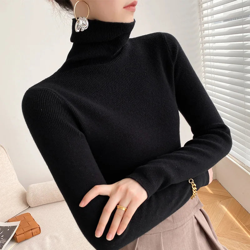Model wears the fine-knit turtleneck jumper in black with a pleated skirt, arms crossed 8