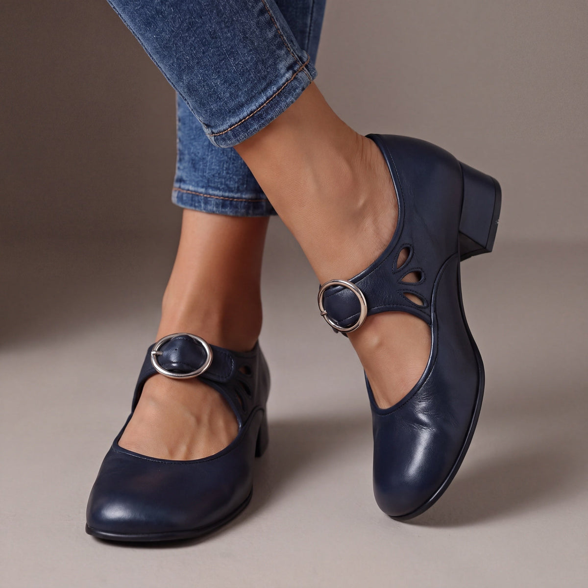 Navy blue leather block-heel pumps worn with cropped jeans, showing a round silver buckle strap and teardrop cut-outs on the side. 4