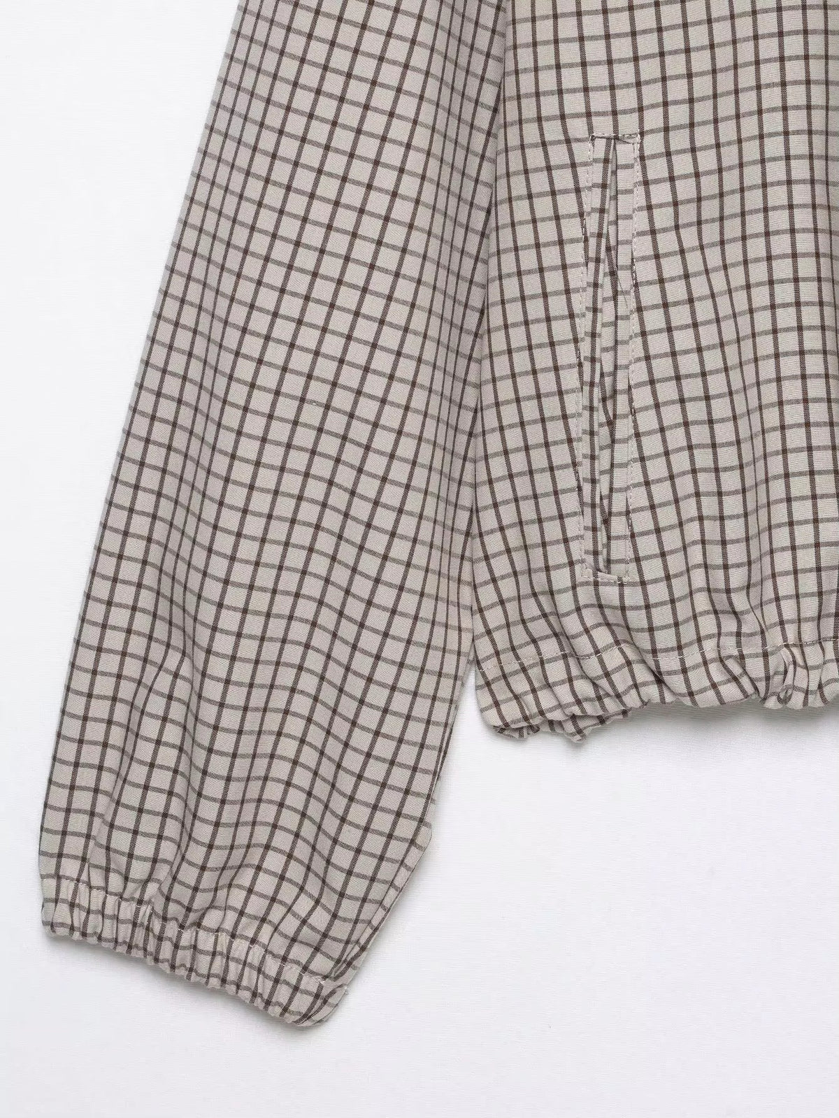 Detail of the checked sleeve with elasticated cuff and a side pocket above the gathered hem, laid flat. 8