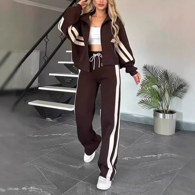 Model walking in the dark brown set with cream side stripes and drawstring waist, beside a staircase and potted plant. 8