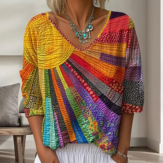 Close-up of the V-neck blouse in bright yellow, orange, red and purple patchwork with a sunburst design, worn with a turquoise necklace. 1