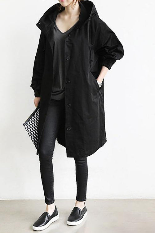 Black hooded button-front coat worn open over a dark top, with leggings, slip-on shoes and a patterned clutch 2