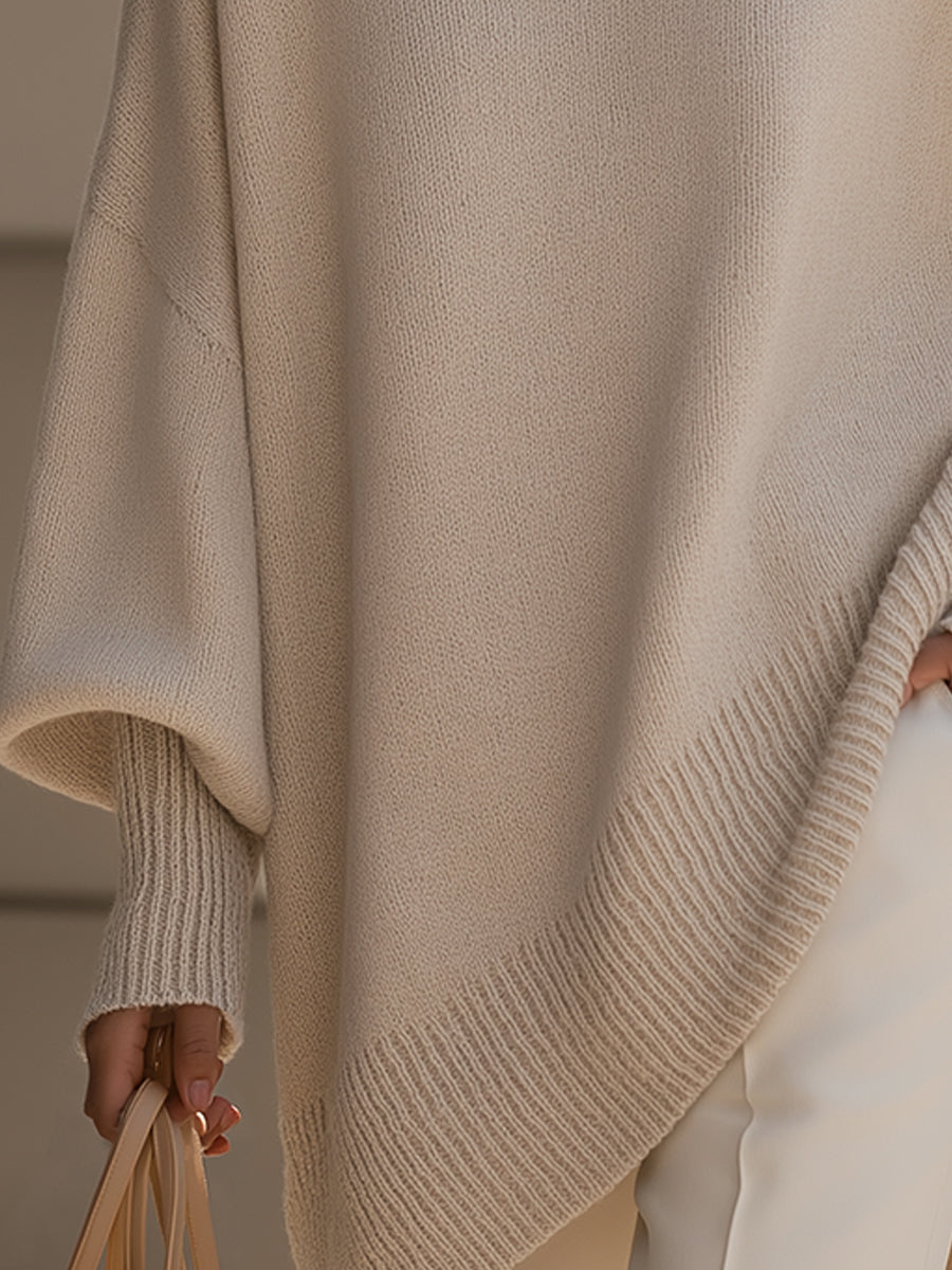 Close-up of the beige poncho's ribbed asymmetric hem and ribbed cuff on a draped sleeve 4