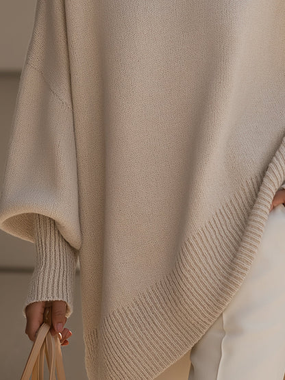 Close-up of the beige poncho's ribbed asymmetric hem and ribbed cuff on a draped sleeve 4